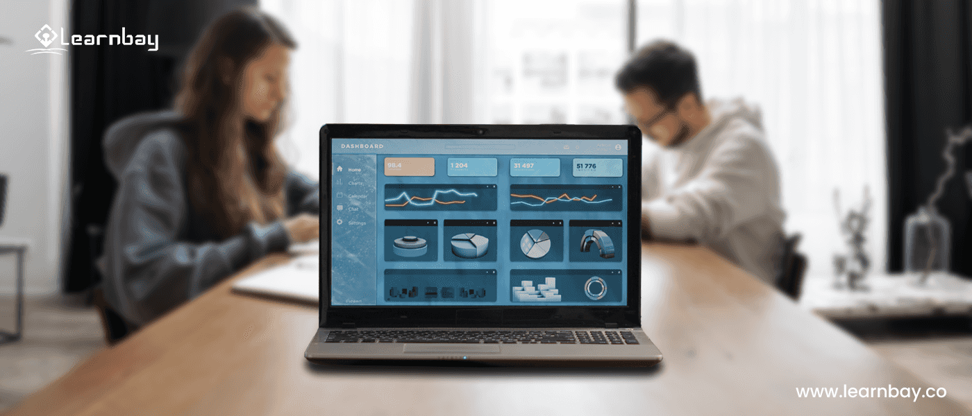 A laptop on a table shows various analytical data in the foreground. The blurred background shows two data analysts seated at the same table, working.